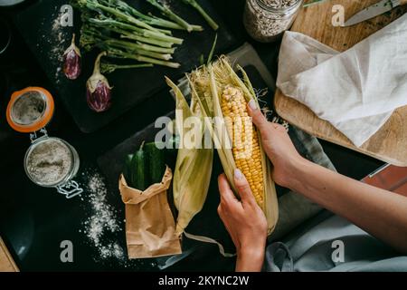 Directly above view of female chef peeling fresh corn at studio kitchen Stock Photo