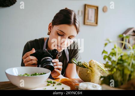 Food stylist adjusting camera lens while photographing green peas in studio Stock Photo