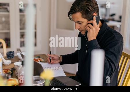 Young businessman talking on smart phone while working from home Stock Photo