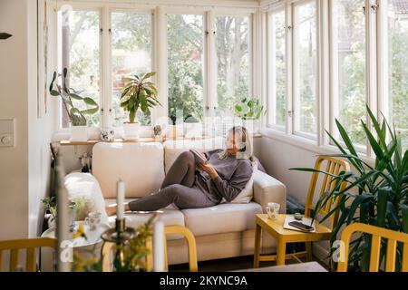 Businesswoman with book reclining on sofa in living room at home Stock Photo