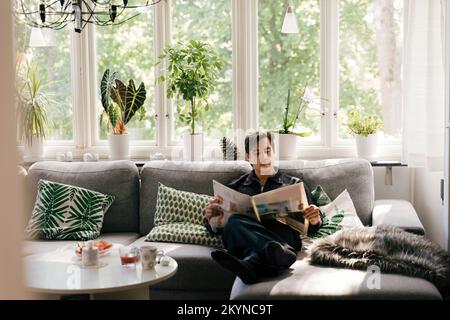Young man reading newspaper while sitting on sofa in living room at home Stock Photo