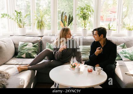 Worried couple talking to each other while sitting on sofa in living room Stock Photo