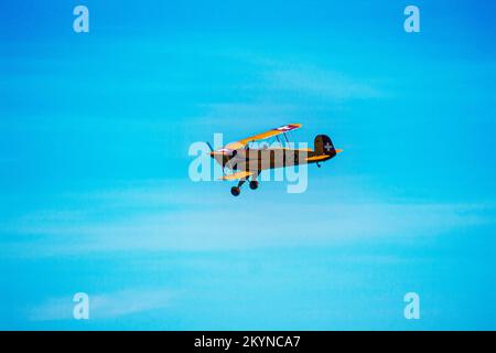 A small yellow airplane flying against a blue sky Stock Photo