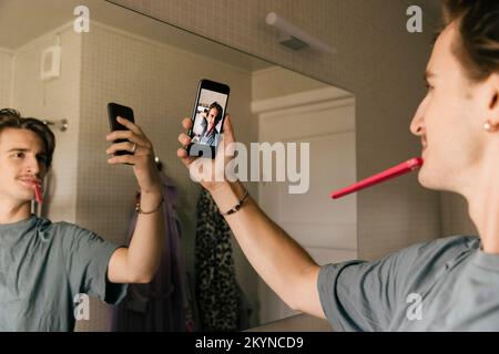 Man brushing teeth taking selfie through mobile phone in bathroom at home Stock Photo