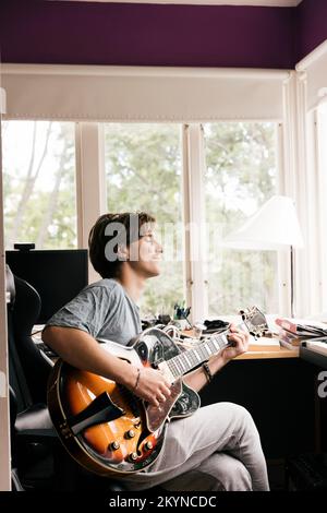 Young man with eyes closed playing guitar while sitting at home Stock Photo