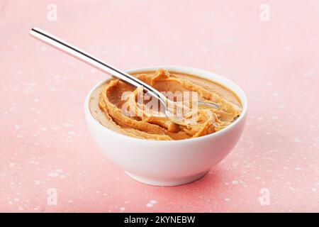 smooth peanut butter in bowl on pink background Stock Photo