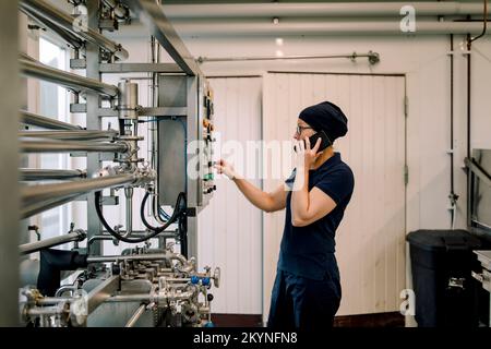 Farmer operating machine and talking on smart phone at dairy factory Stock Photo