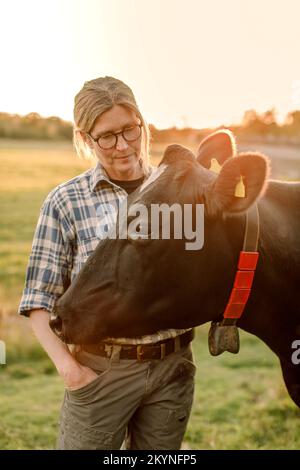 Female farmer standing by cow at field during sunset Stock Photo