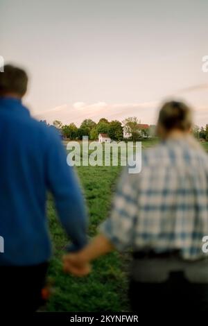 Mature couple holding hands and walking on field Stock Photo