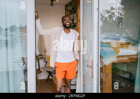 Smiling mature man with hand in pocket standing at doorway Stock Photo