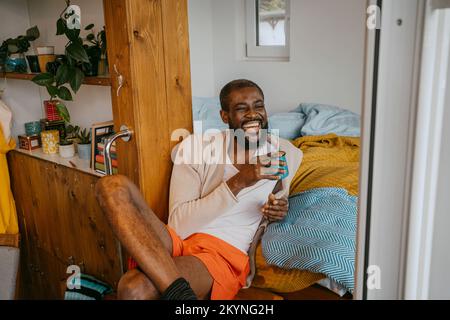 Happy mature man with coffee cup sitting with legs crossed at home Stock Photo