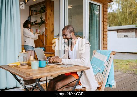 Happy mature man using laptop while sitting at table on porch outside house Stock Photo