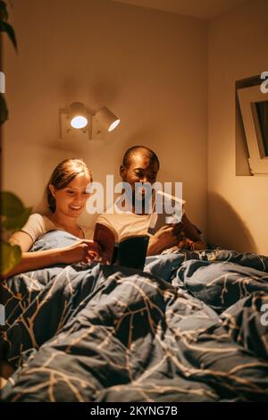 Man and woman reading books while resting on bed with blanket at home Stock Photo