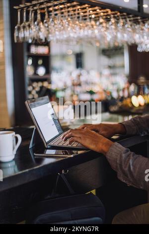 Hands of businessman typing on laptop at bar counter in restaurant Stock Photo