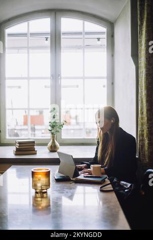 Female freelancer using laptop while sitting at table in restaurant Stock Photo
