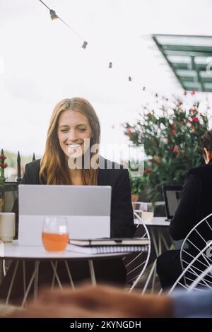 Happy female professional sitting with laptop at cafe Stock Photo