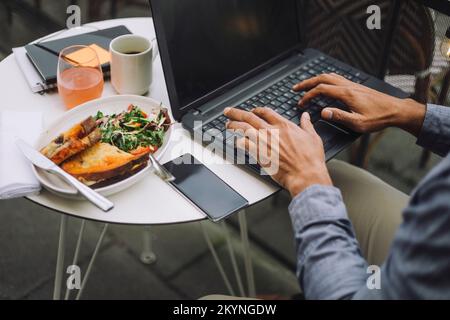 Hands of businessman using laptop by meal and smart phone on table Stock Photo