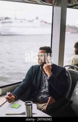 Businessman taking on mobile phone while traveling in ferry Stock Photo