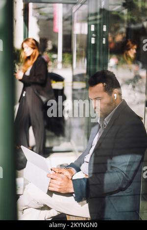Businessman using laptop while sitting at bus stop during sunny day Stock Photo