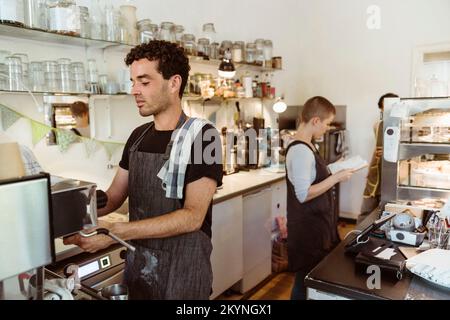 Male barista preparing coffee using coffee maker in cafe Stock Photo