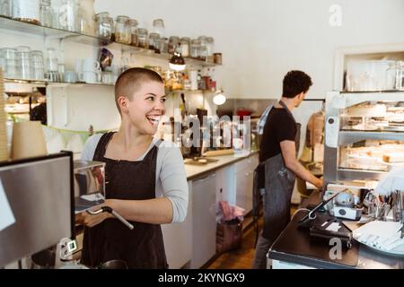 Young happy female owner looking away while preparing coffee in cafe Stock Photo