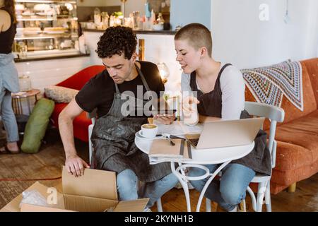 Male and female owners checking box while sitting on chair in cafe Stock Photo