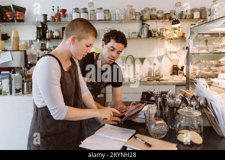 Male and female owners doing inventory using tablet PC at cafe Stock Photo