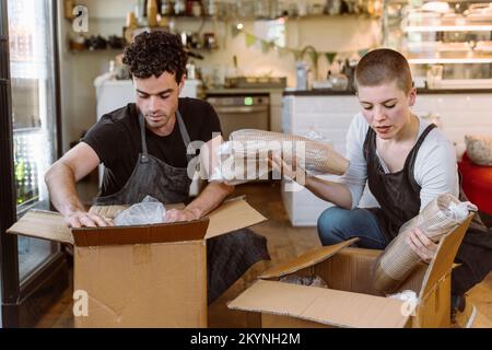 Male and female owners unboxing disposable cups from cardboard boxes at cafe Stock Photo