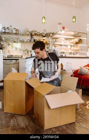 Male owner checking inventory in cardboard boxes at cafe Stock Photo
