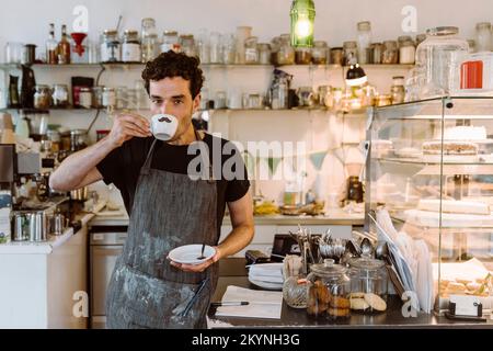 Male owner drinking coffee while standing near counter in cafe Stock Photo