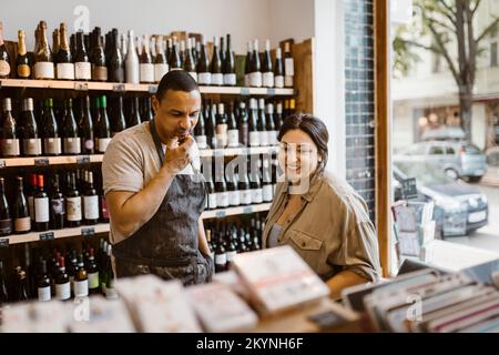 Male owner with hand on chin standing with female colleague at wine shop Stock Photo