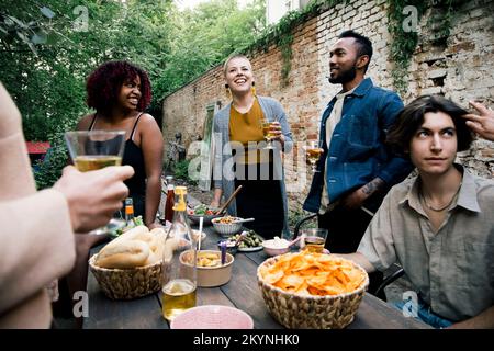 Multiracial male and female friends enjoying food and drinks at garden party Stock Photo