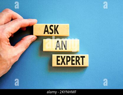 Ask an expert symbol. Concept words Ask an expert on wooden blocks on a beautiful blue table blue background. Businessman hand. Business and ask an ex Stock Photo