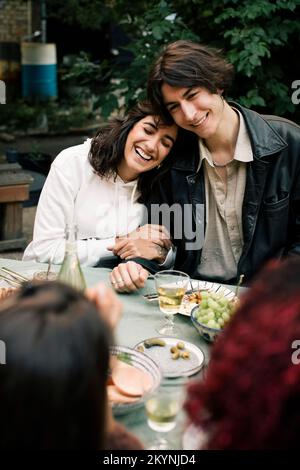 Happy woman leaning on man's shoulder during dinner party in back yard Stock Photo