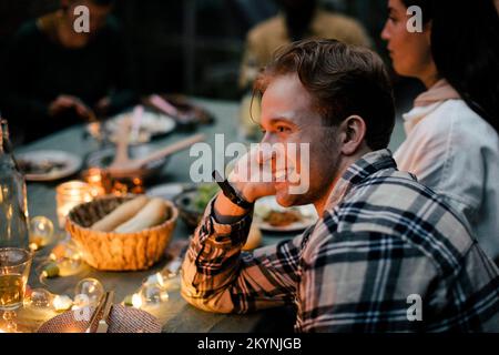 Side view of smiling young man leaning on elbow at dining table during sinner party Stock Photo