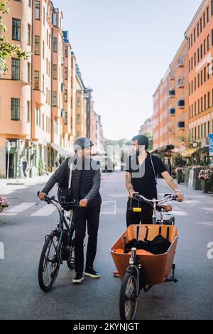 Male business colleagues with bicycles talking while standing on road Stock Photo