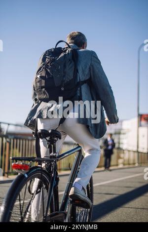 Rear view of businessman with backpack riding bicycle on road Stock Photo