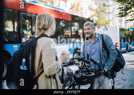 Male and female business colleagues with bicycles talking to each other at street Stock Photo