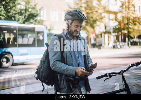 Smiling businessman wearing cycling helmet using mobile phone Stock Photo