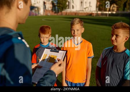 Football trainer talking to team of little players on field during break Stock Photo