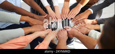 Multiracial men and women put their hands together in circle as symbol of cooperation and unity. Stock Photo
