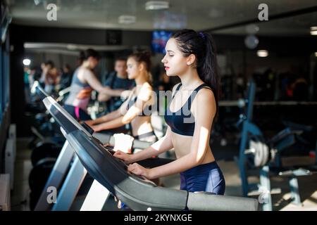 Attractive young sports woman is working out in gym. Doing cardio training on treadmill. Running on treadmill. High quality photo Stock Photo