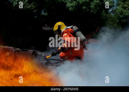 Firefighter Rescue training to stop burning flame, Fireman wear hard hat and safety uniform suit for protection burn using axe to break in a car to re Stock Photo