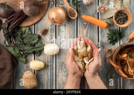 Human hands hold handful of peeled potato peel, flat lay. Mix of raw fresh organic vegetables on wooden table. Healthy food, ingredients for cooking. Stock Photo