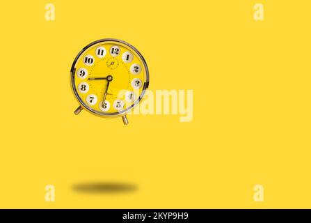 Round yellow alarm clock flying above the ground as a concept for time flies or wake up alarm on a bright yellow background with space for copy Stock Photo