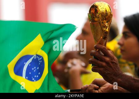 Fifa World Cup trophy replica close up detail and brazilian flag. Soccer fan hand holding award in celebration, supporting national football team Stock Photo