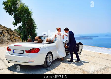 Beautiful young couple bride and groom posing near white cabriolet on Santorini island Stock Photo