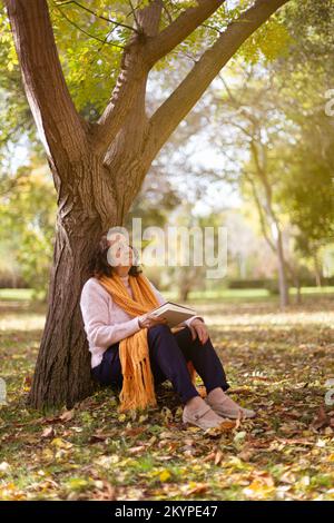 Elderly caucasian woman resting by a tree outdoors. Autumn season. Space for text. Stock Photo