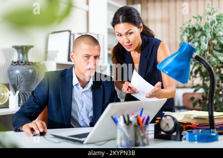 Upset office employe looking on laptop with disgruntled female manager Stock Photo