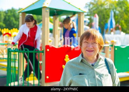 Grandmother walks with her grandchildren on playground Stock Photo